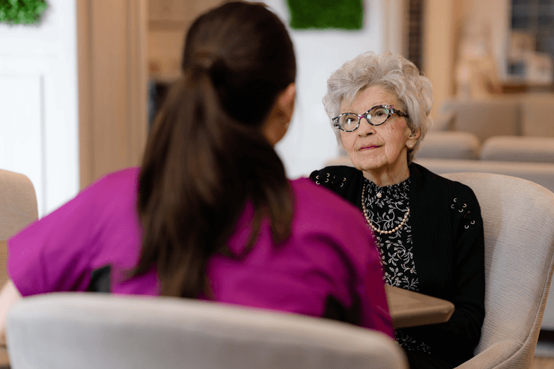 Senior woman sitting down talking with Chartwell staff member. Femme âgée assise discutant avec un membre du personnel de Chartwell.